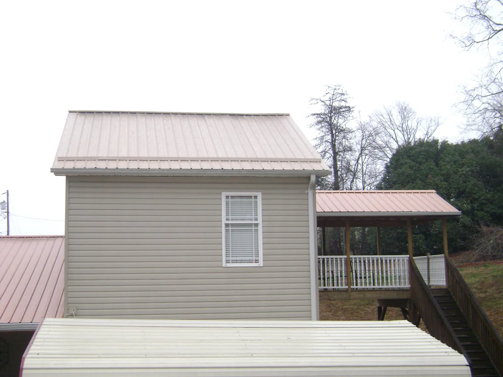 Tan metal roofs on a two story addition and attached porch, from a Roof Replacement job in Collins